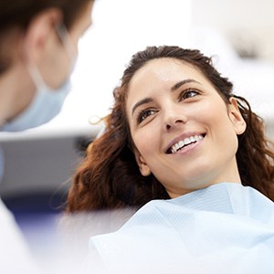 A smiling young woman leaning back in a dental chair and looking at her dentist