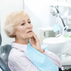 senior dental patient holding her cheek in pain