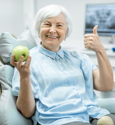 smiling senior woman holding apple after dental implant salvage in Bettendorf