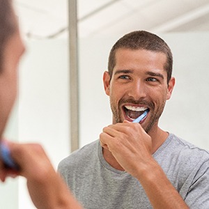 man in grey shirt brushing his teeth in front of a mirror