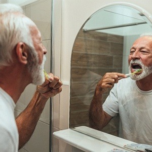 older man brushing his teeth in front of a mirror