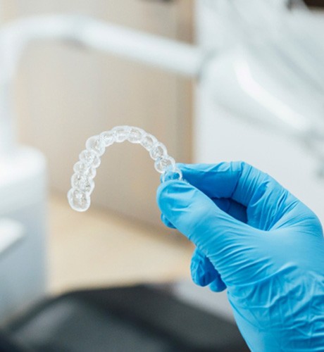 Dentist with blue glove holding clear aligner