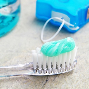 Toothbrush with toothpaste next to mouthwash and dental floss