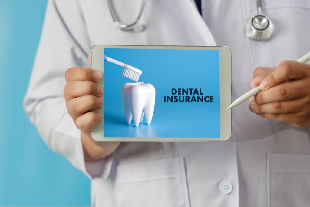 Dentist in white coat holding tablet with dental insurance displayed